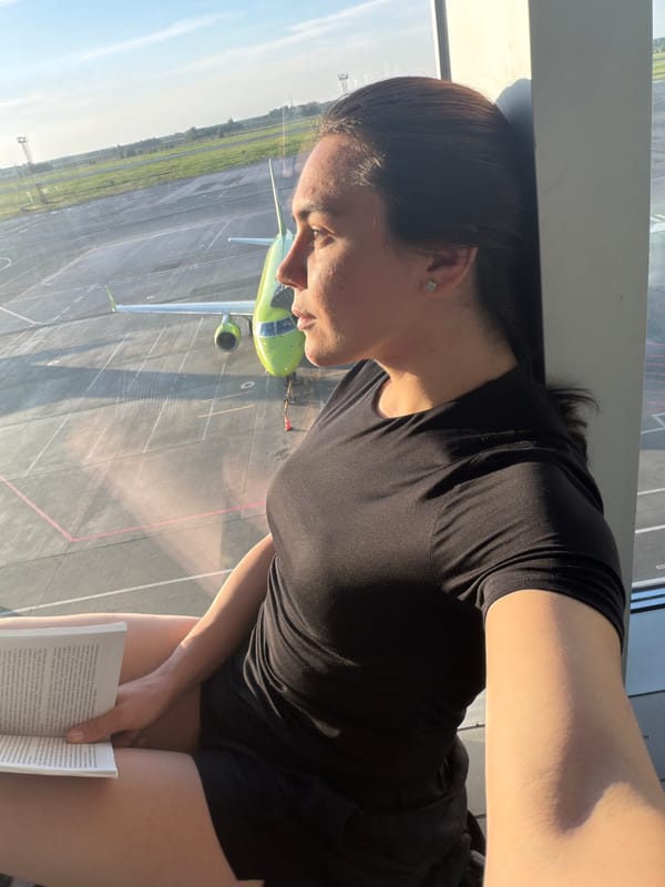 Woman reads book in airport lounge overlooking tarmac