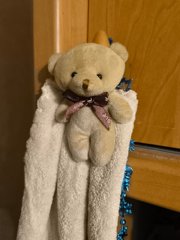 Tan teddy bear with pink-lettered ribbon hanging from wooden surface