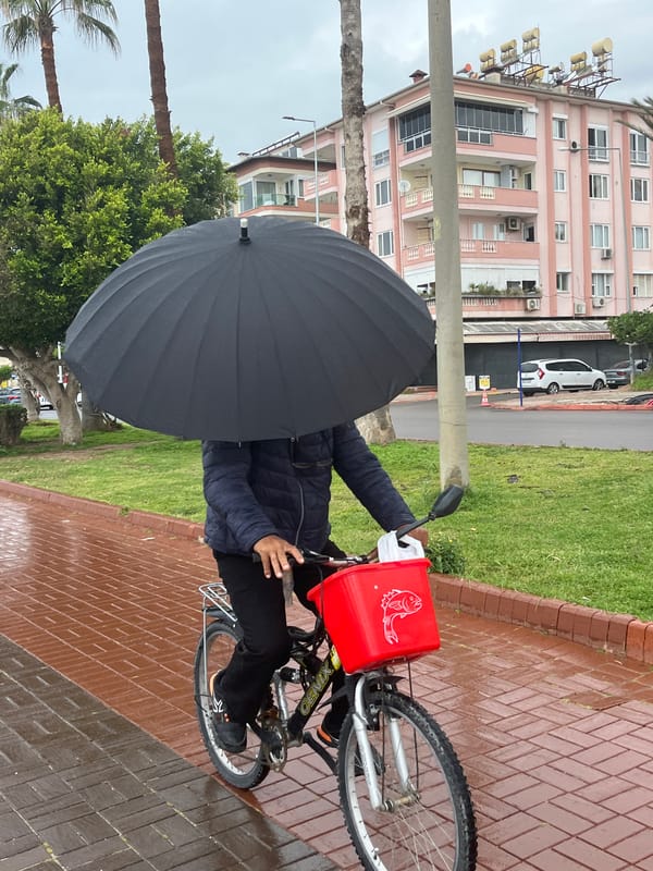 Cyclist rides with umbrella on wet sidewalk in Alanya