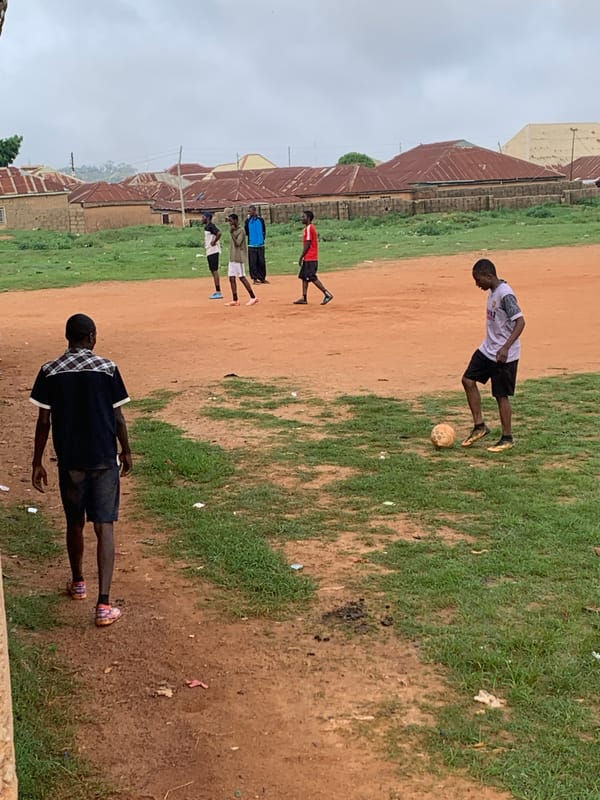 Pickup soccer game on a red dirt field in Bukuru, Nigeria.