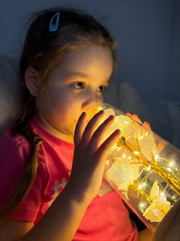 Girl plays with illuminated artificial flowers in glass container
