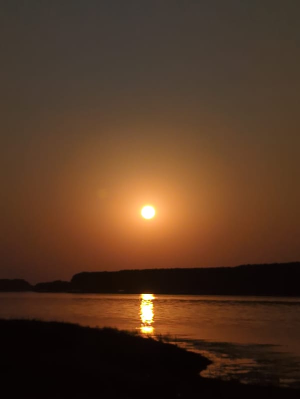 Orange sun low over calm water, sky fading to blue