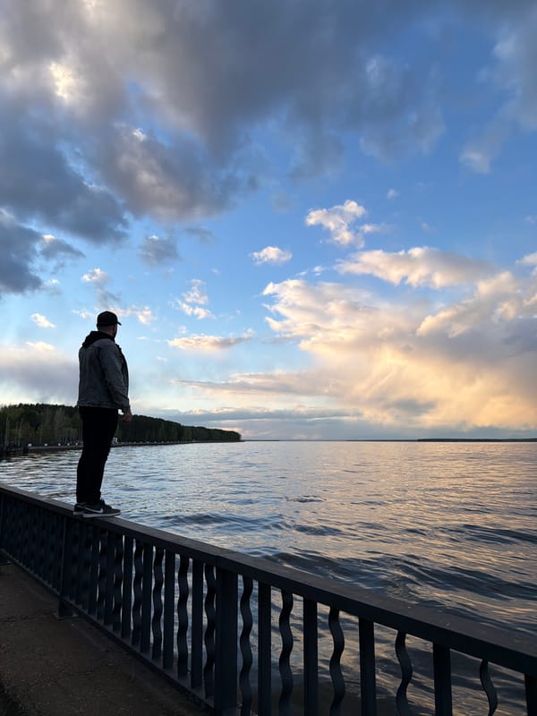 Man stands on bridge railing overlooking water in Chaikovsky