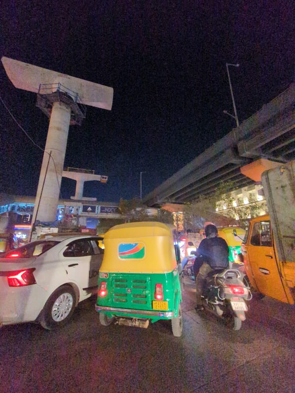 Auto-rickshaw parks beside white car on busy Bengaluru street