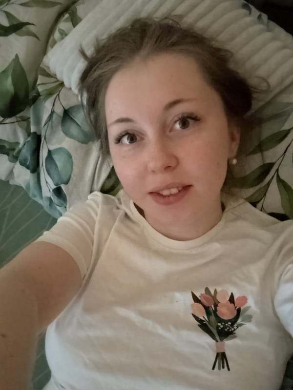 Woman rests on patterned bed in white floral shirt