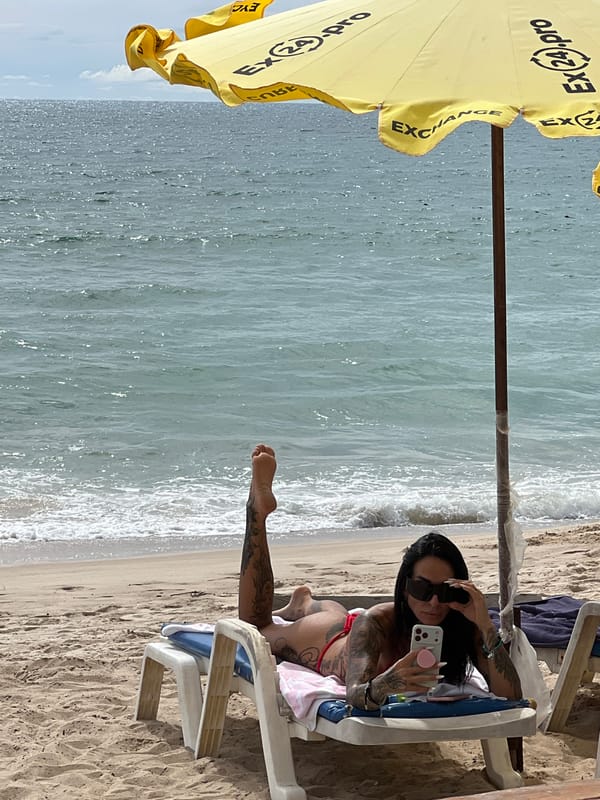 Beach day under a branded umbrella, phones out, waves in background.