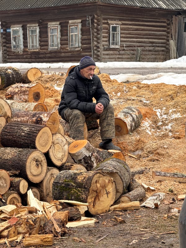 Family gathered around log pile in rural Russian village