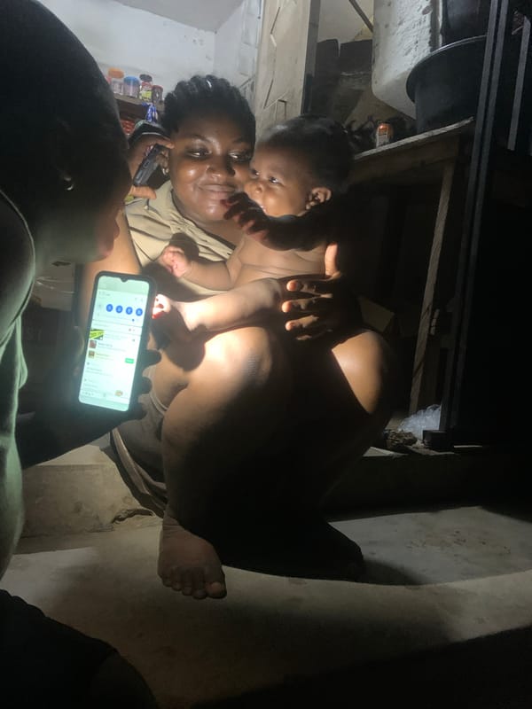 Woman with baby uses phone near shop in Lokoja