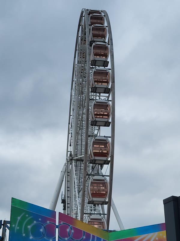 Large white Ferris wheel operates under partly cloudy skies