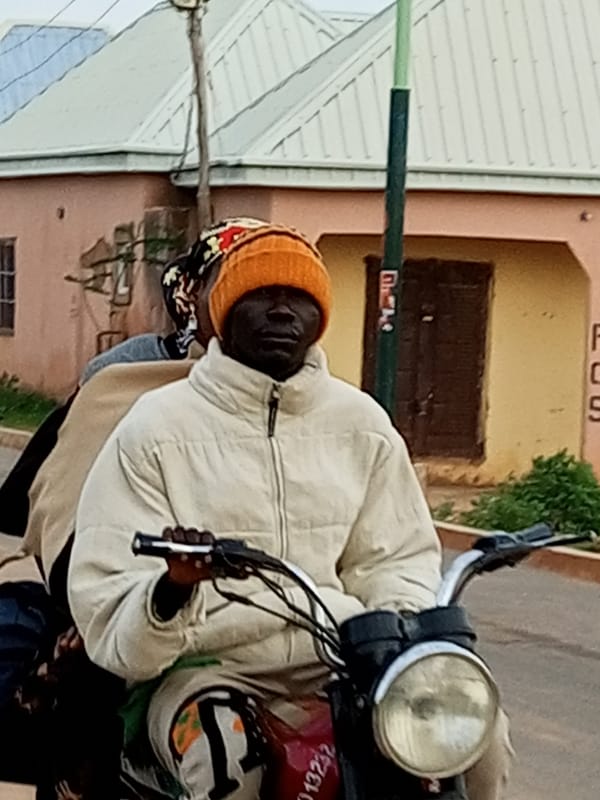 Foot traffic and a motorcycle near a blue gate on a dirt path