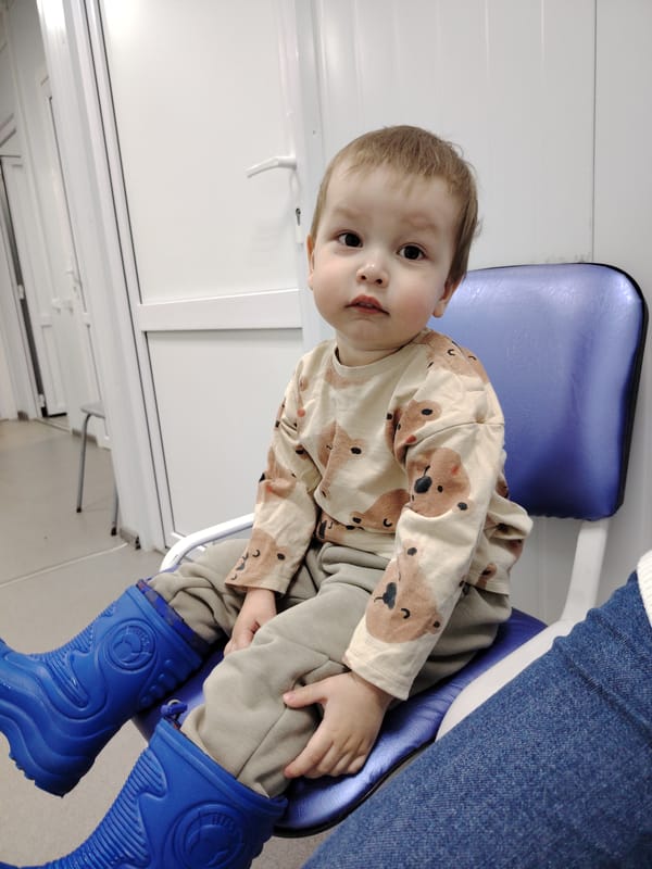 Child in rain boots sits apprehensively on blue chair