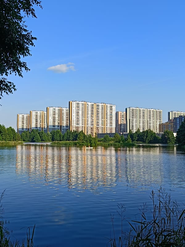 Calm city lake with paddleboarder, reflections, and a ruined waterside structure