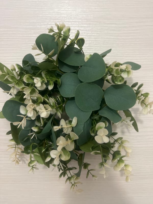 Artificial eucalyptus and white flower arrangement on textured surface.