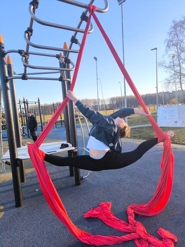 Woman performs aerial silk split on park jungle gym