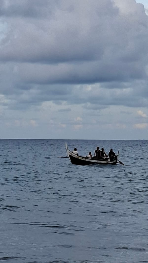 Busy morning at Lhokseumawe's Ujong Blang Beach — swimmers, boats, rocky shore