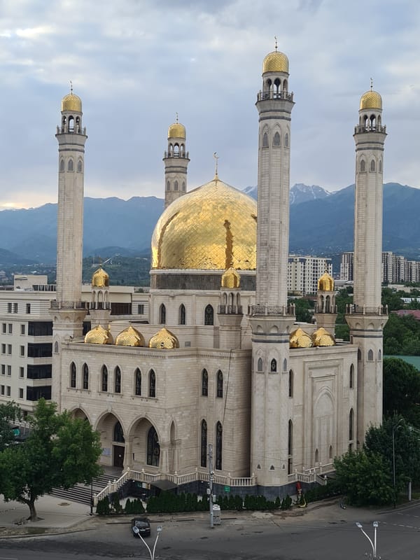 Almaty at dusk: mosque, mountains, and city skyline.