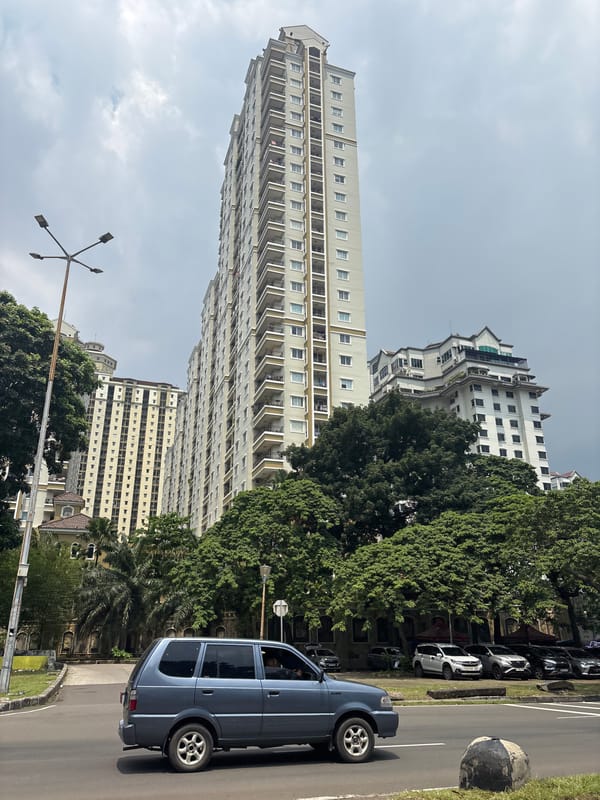 Blue car parked among vehicles on tree-lined Jakarta street