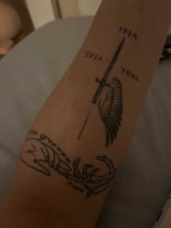 Forearm tattoo with winged sword and Latin phrase displayed in Plovdiv