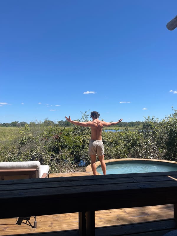 Man stands arms outstretched on deck in Khwai, Botswana