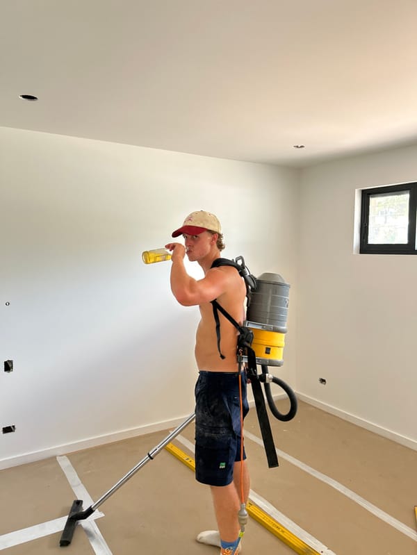 Construction worker vacuums unfinished room while drinking beer in Stanwell Tops