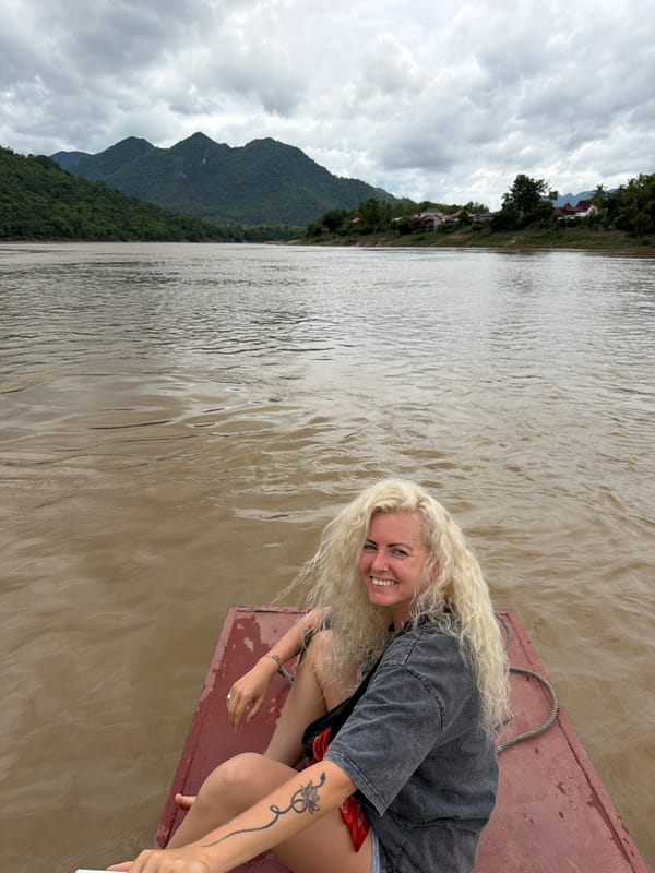 Drifting down a muddy Laotian river on a red wooden boat
