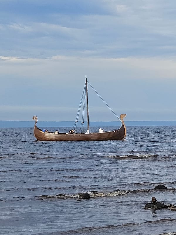 Viking longship sails past a busy waterfront on a grey day