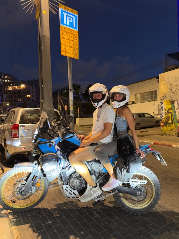 Helmeted duo on a blue motorcycle, Tel Aviv night