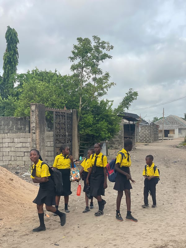 Students in uniforms walk sandy path in Badagry