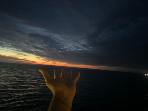 Person photographs twilight vessel from Baltic Sea coastline