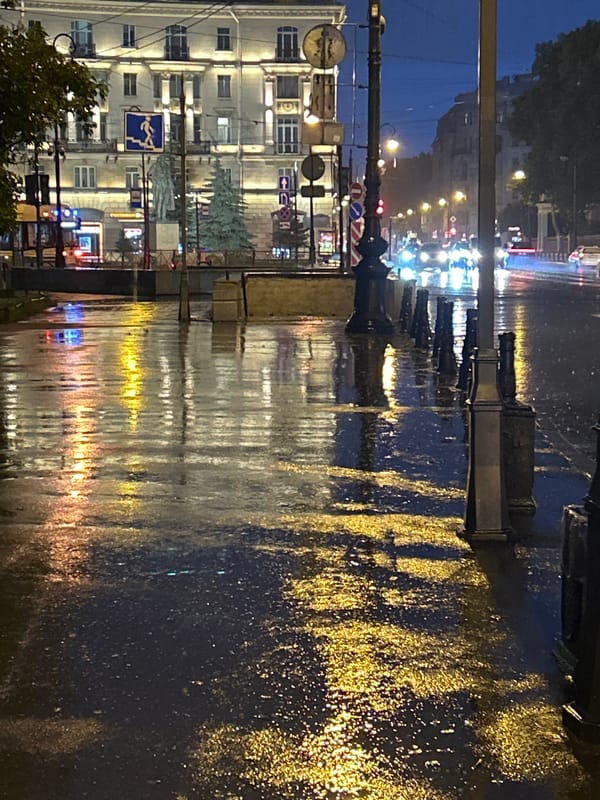 Rainy city evening: wet streets, trams, and a glowing metro entrance