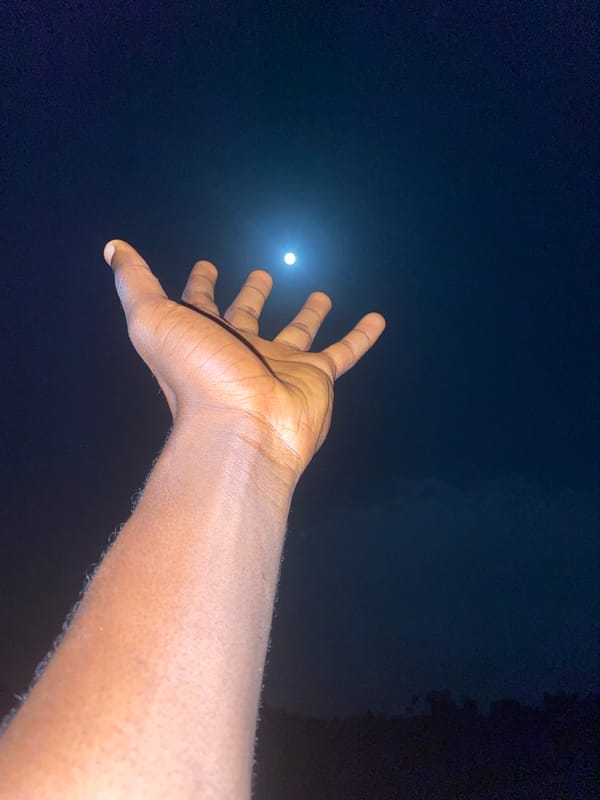 Hand reaching toward the moon on a hazy night in Nigeria