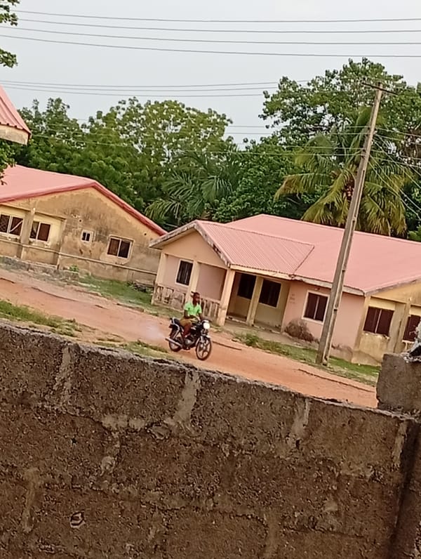 Motorcyclist travels dirt road between red-roofed buildings