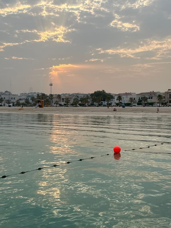Dubai beachfront at golden hour, calm water and cloudy skies