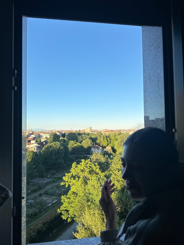 Person observes Milan cityscape from window on clear afternoon