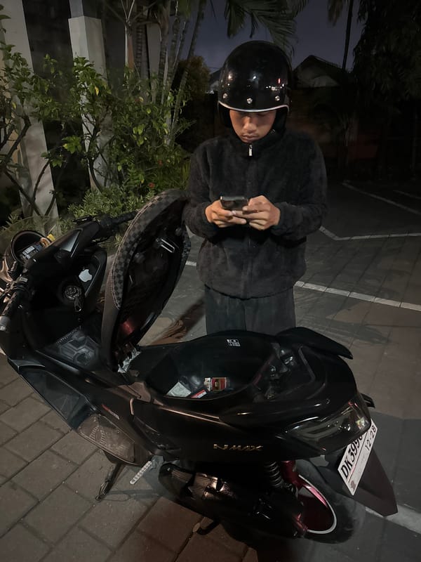 Night stop on a palm-lined Denpasar street, scooter and phone in hand