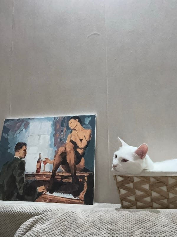White cat sits beside painting in domestic setting