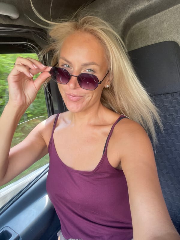 In-car moment, sunglasses in hand, looking at the camera.