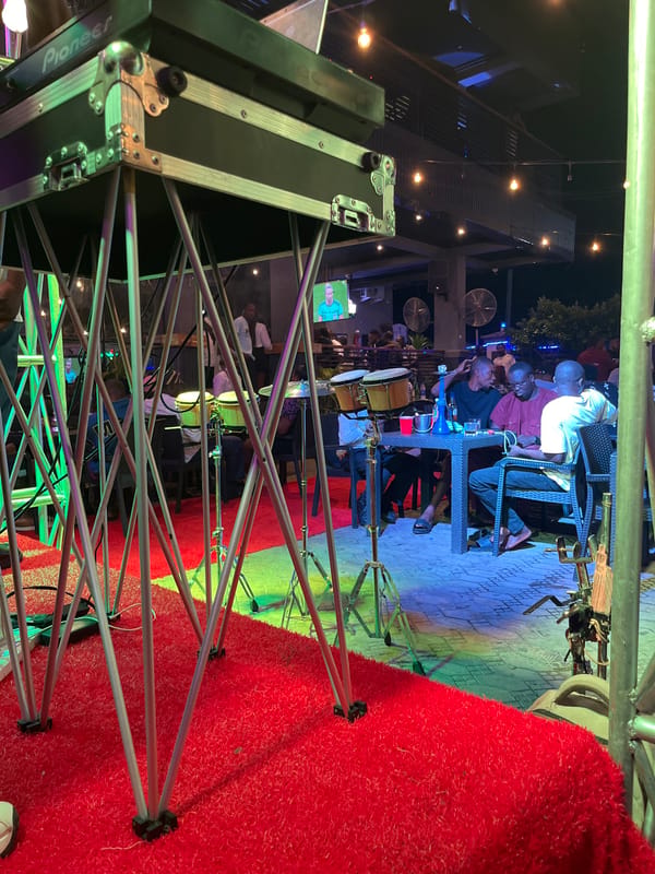 Outdoor bar night with DJ set, live drums, and string lights