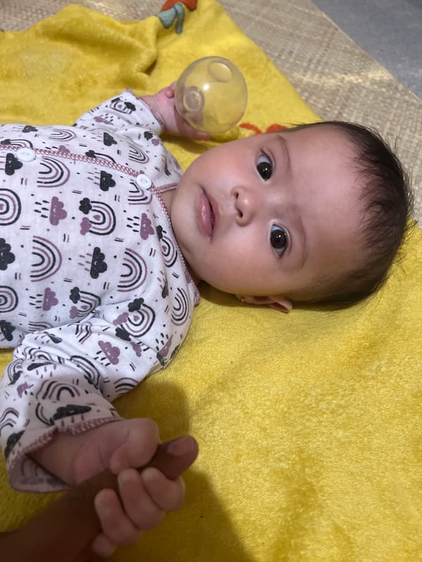 Baby on yellow blanket, rainbow onesie, Lhokseumawe