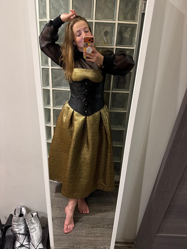 Woman takes mirror selfie in black and gold outfit