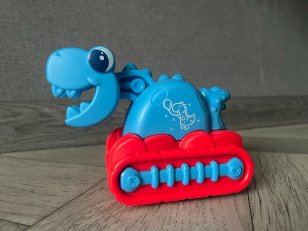 Toy dinosaur bulldozer and gray cat observed in domestic setting