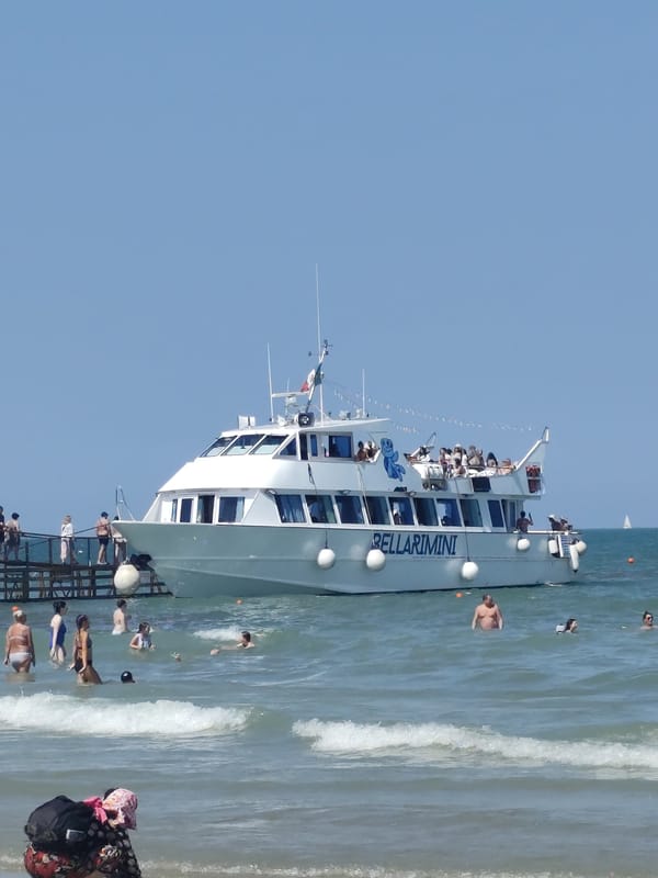 Kites, crowds, and a tourist boat on Rimini's summer beach
