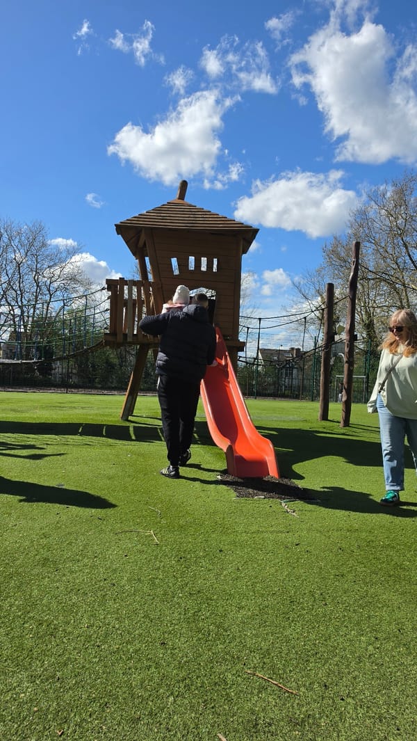 Toddler plays on London playground slide with adult assistance