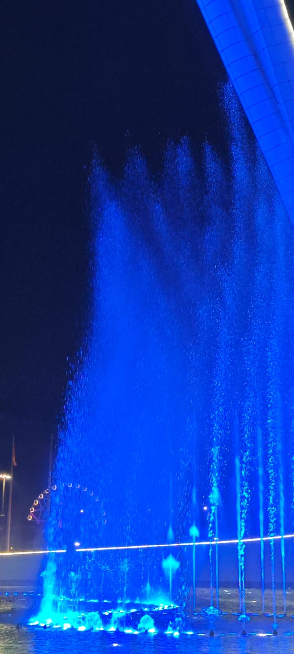 Blue fountain display observed with distant Ferris wheel visible