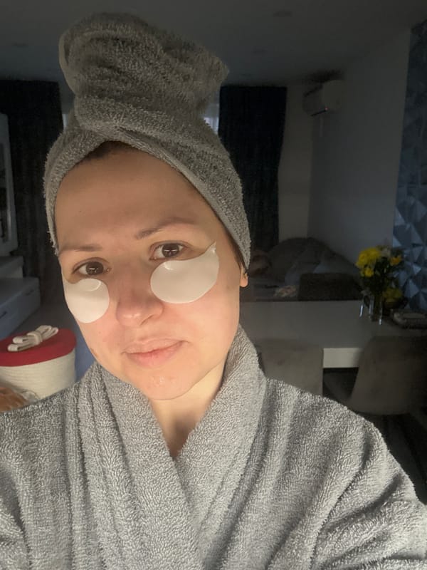 Woman in bathrobe with facial patches holds mug indoors