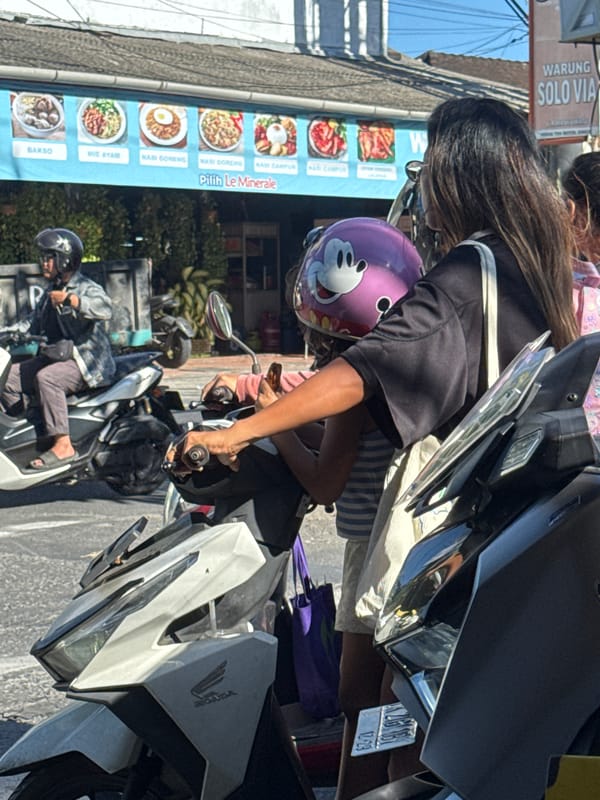 Morning scooter traffic flows past a roadside deity statue in Kuta Selatan