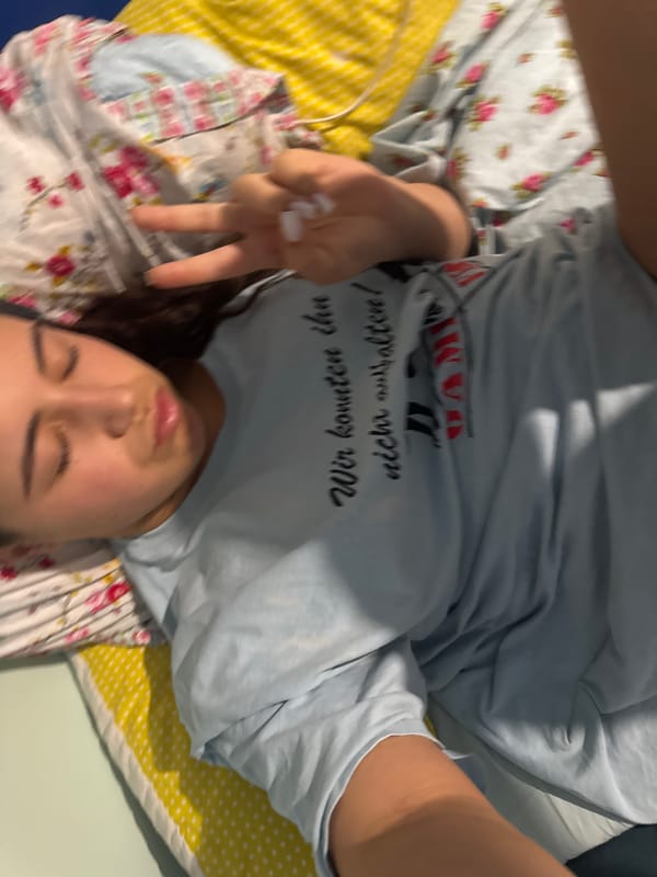 Person makes peace sign on bed wearing graphic t-shirt