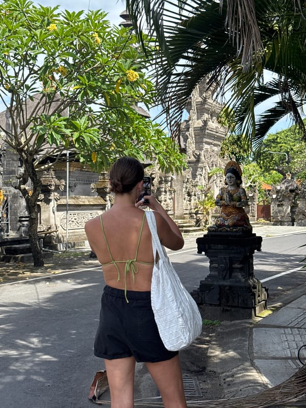 Woman photographs stone statue near carved building in Mengwi