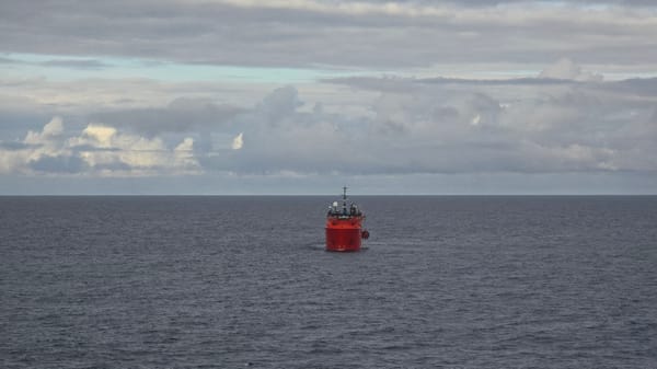 Red ship spotted on calm waters under grey skies