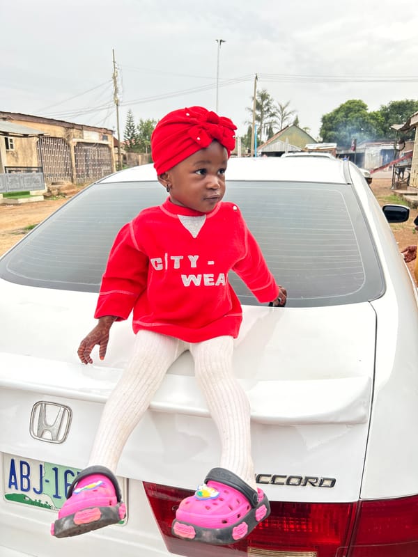 Child in traditional dress poses on car in Jos